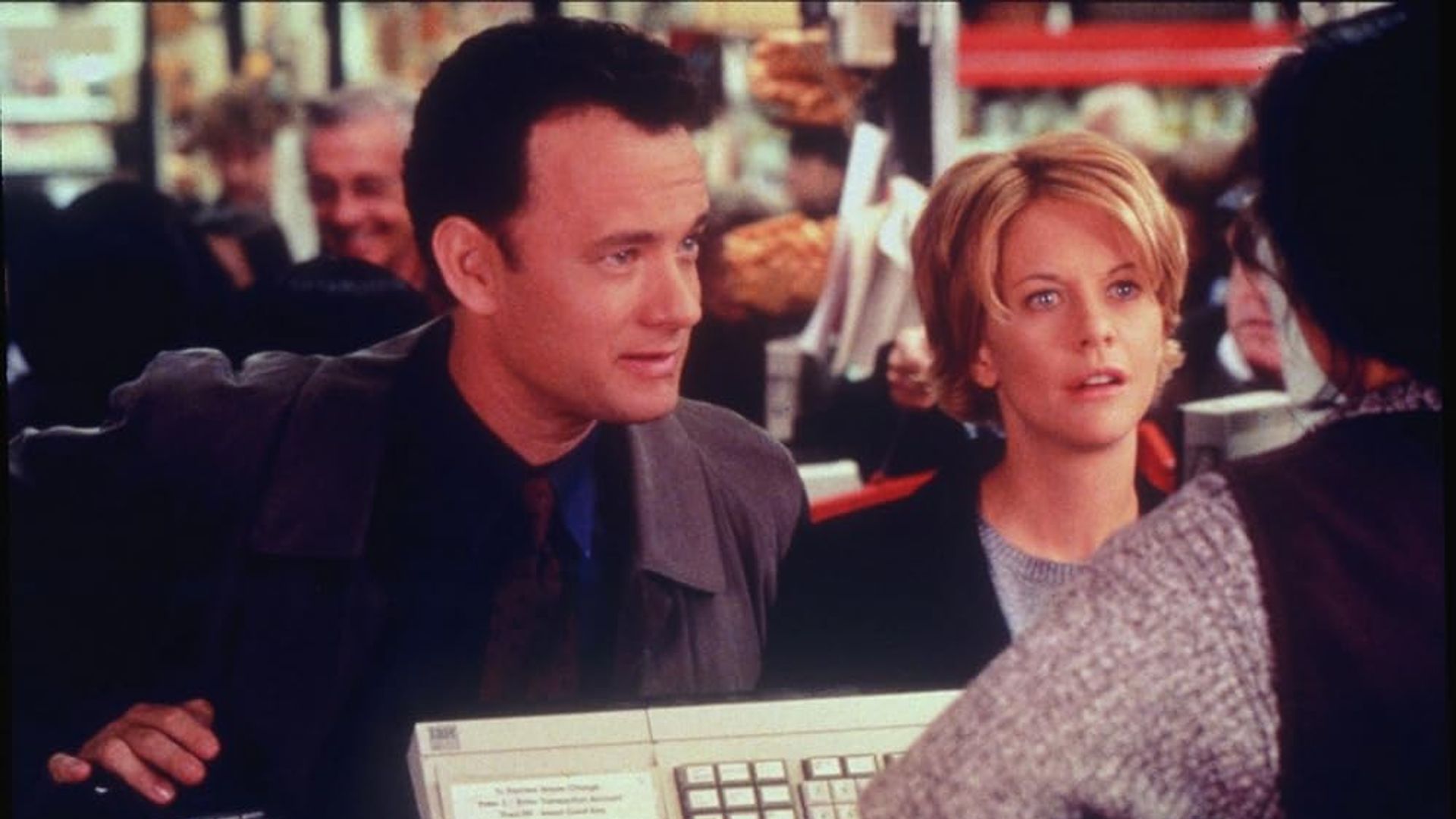 Tom Hanks e Meg Ryan in piedi alla cassa di un negozio mentre parlano con il cassiere