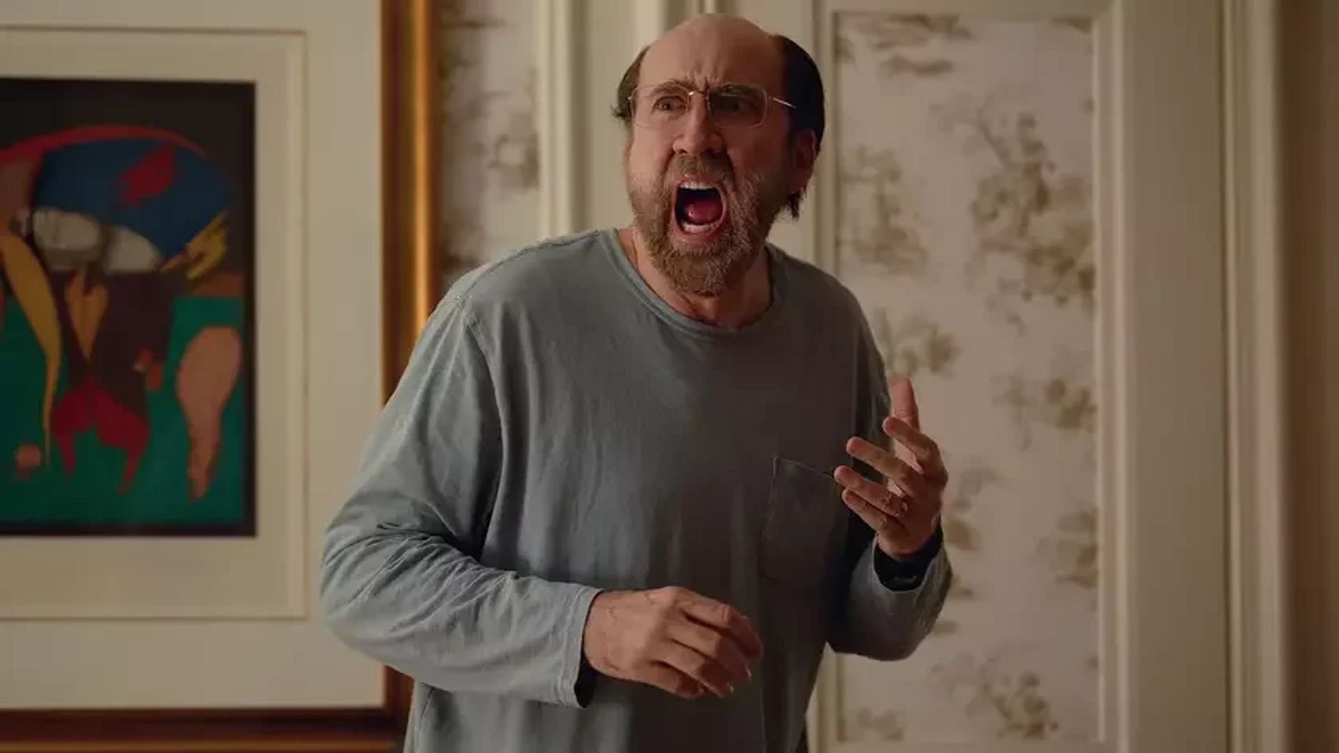 Nicolas Cage con occhiali e una maglietta grigia a maniche lunghe che urla mentre si trova in una stanza