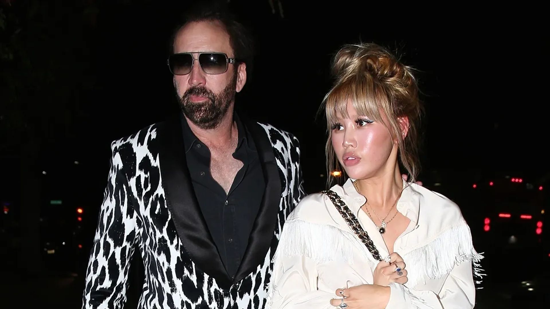 Nicolas Cage in un blazer fantasia bianco e nero ed Erika Koike in una camicetta bianca che camminano insieme di notte