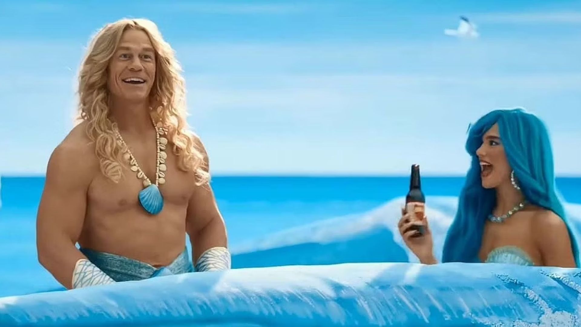 John Cena e Dua Lipa in costumi da sirena che nuotano attraverso onde dipinte