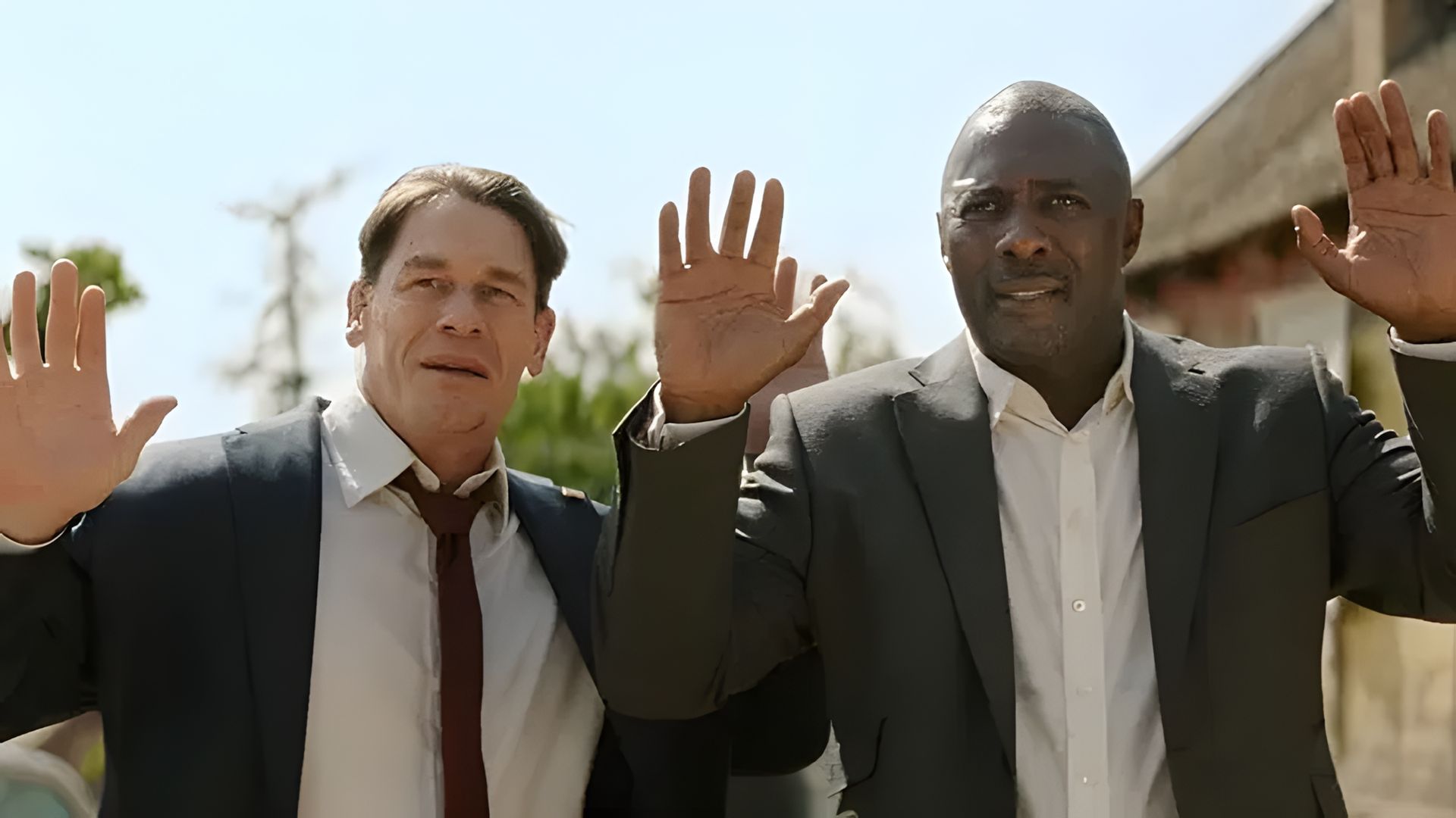 John Cena e Idris Elba in completo che alzano le mani, scena di un film d'azione