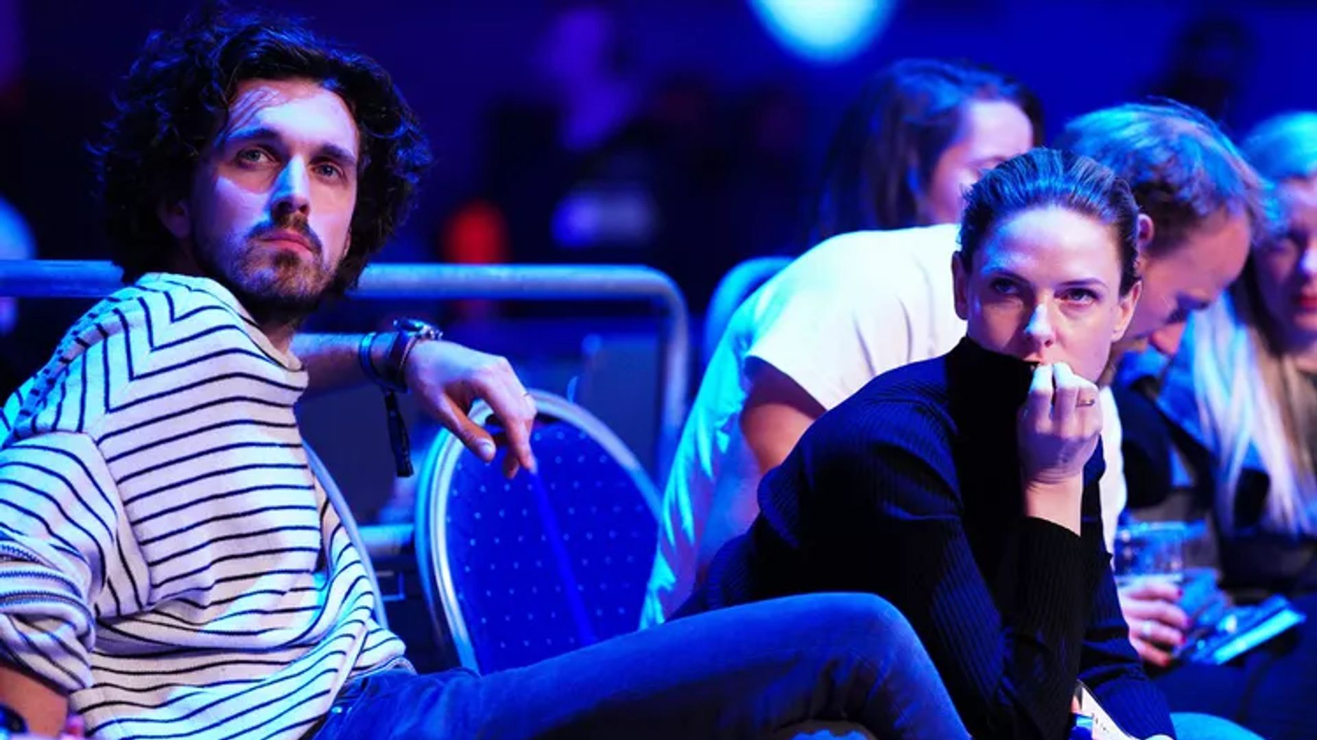 Rebecca Ferguson e Rory St. Clair Gainer seduti in una sala con illuminazione al neon