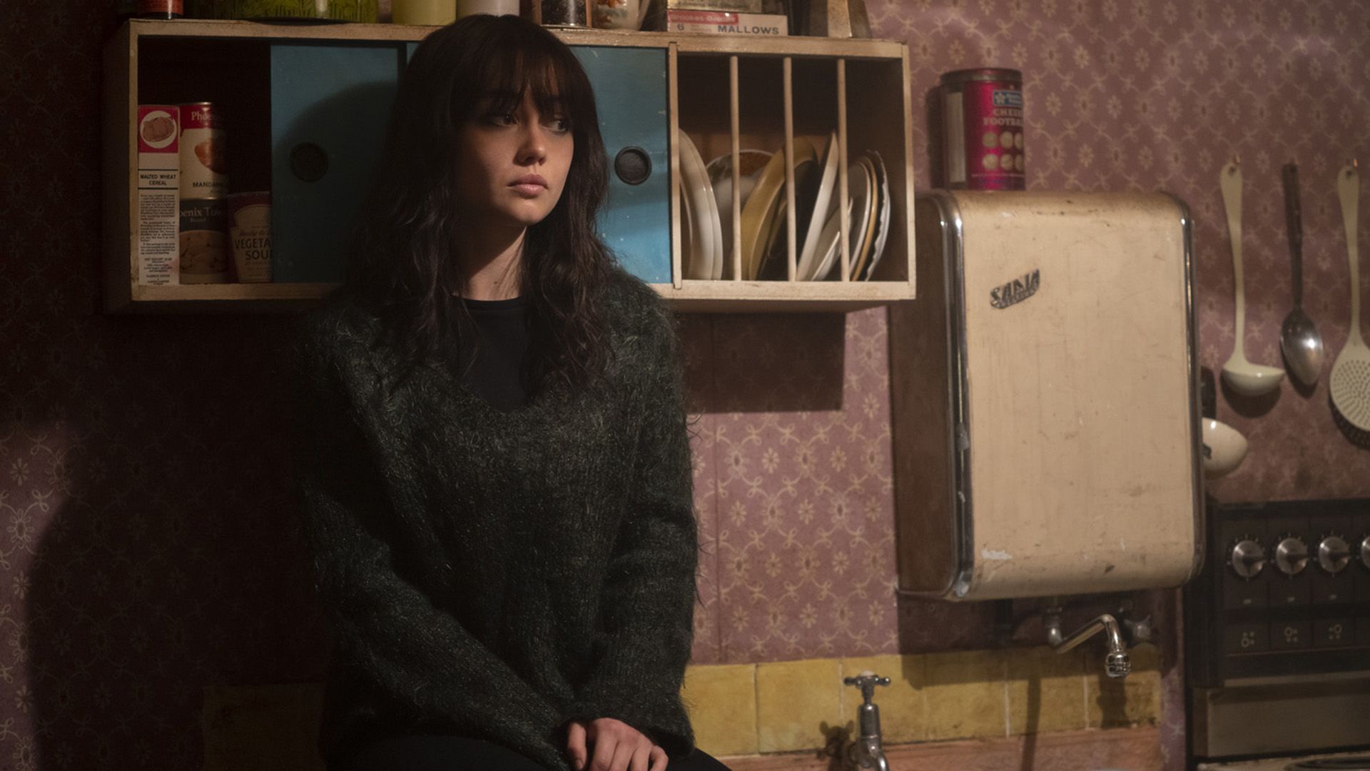 Sydney Chandler in un maglione nero soffice seduta sul tavolo della cucina
