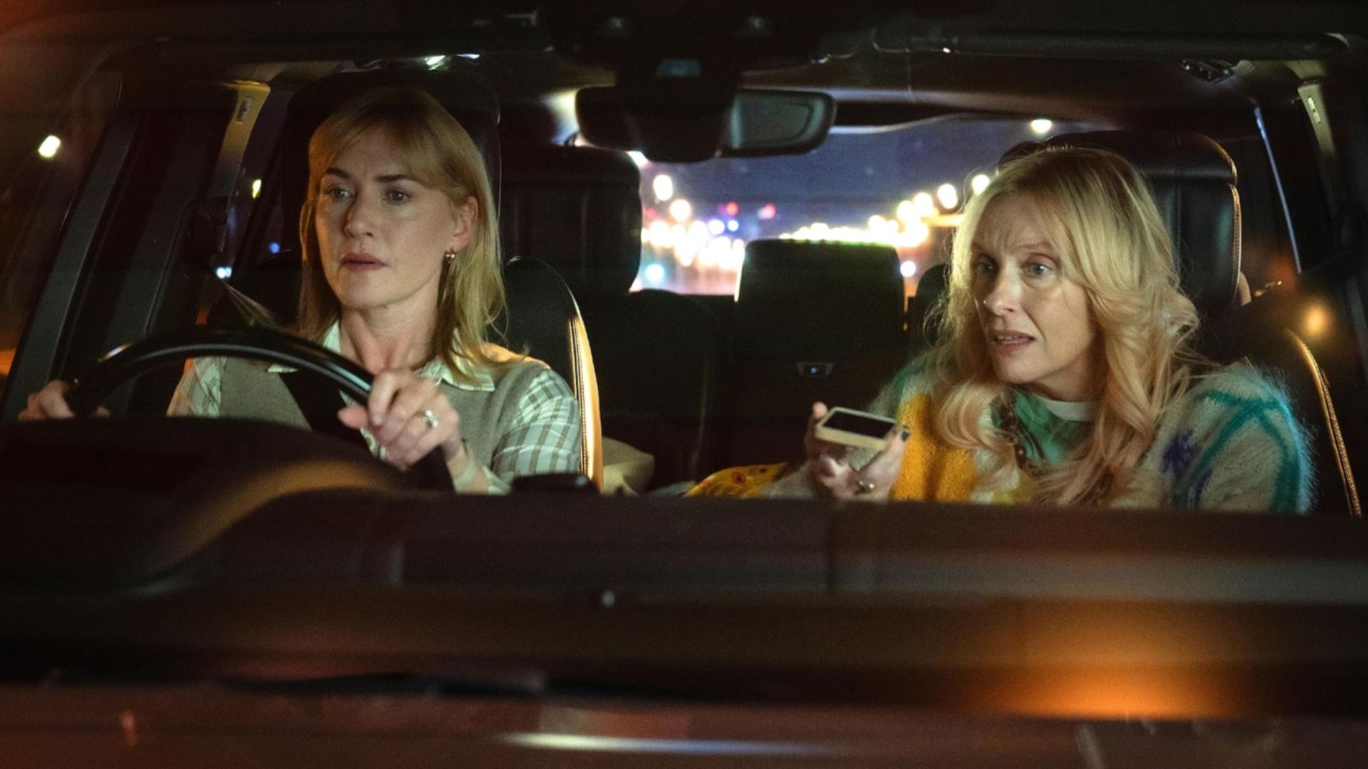 L'attrice Kate Winslet seduta al volante di un'auto mentre l'attrice Toni Collette parla al telefono accanto a lei