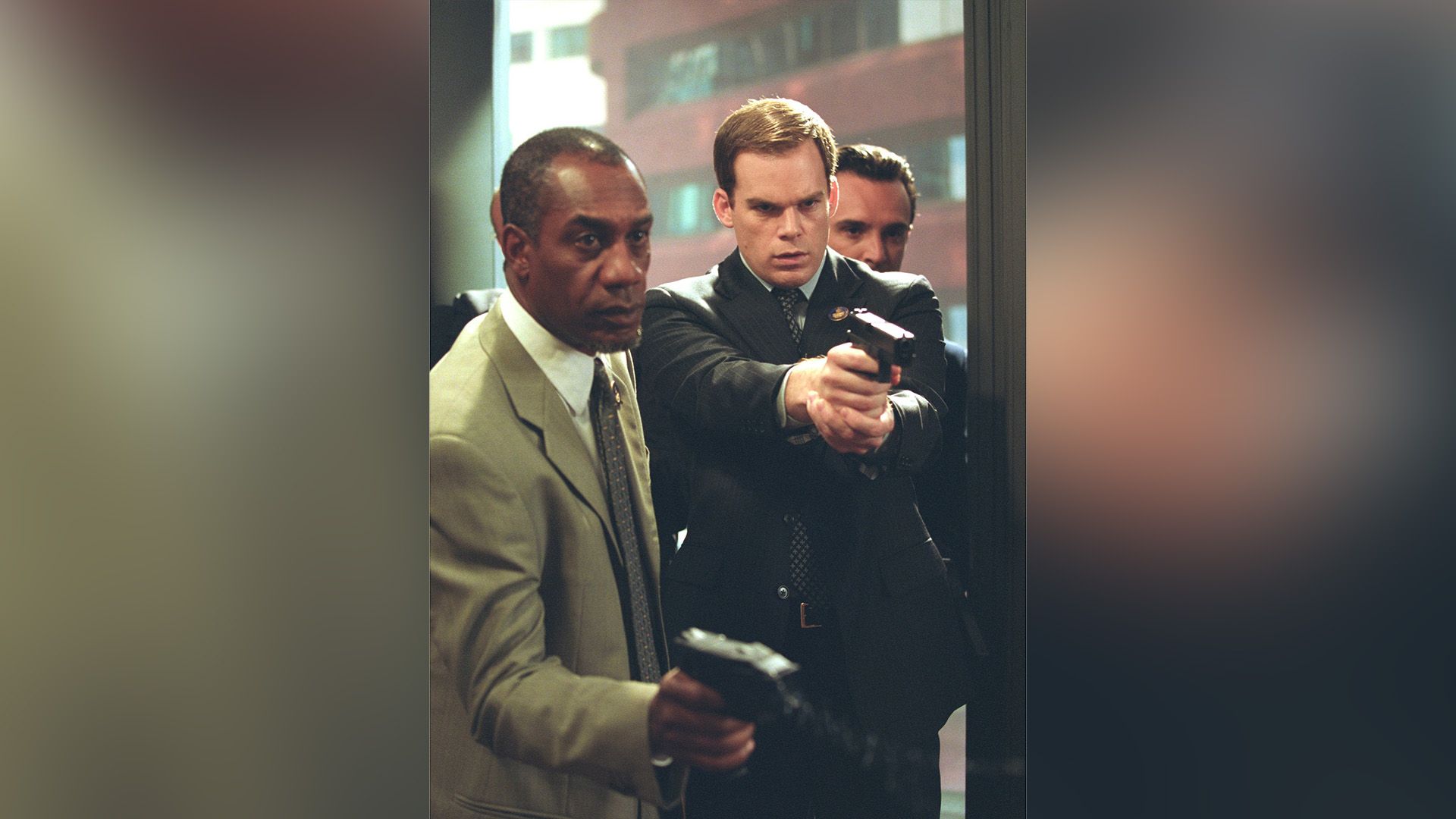 Michael C. Hall e un uomo di colore in piedi con le braccia tese che impugnano delle armi