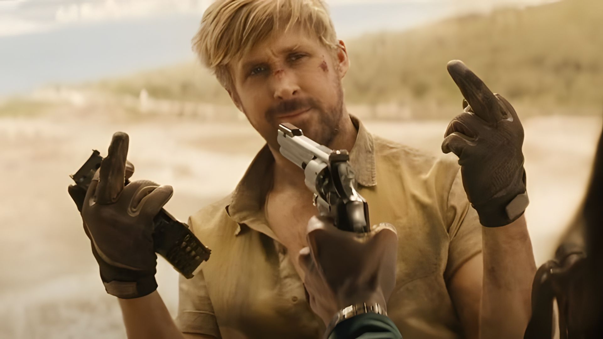 Ryan Gosling con il viso contuso fa un gesto osceno mentre una pistola è puntata contro la sua faccia