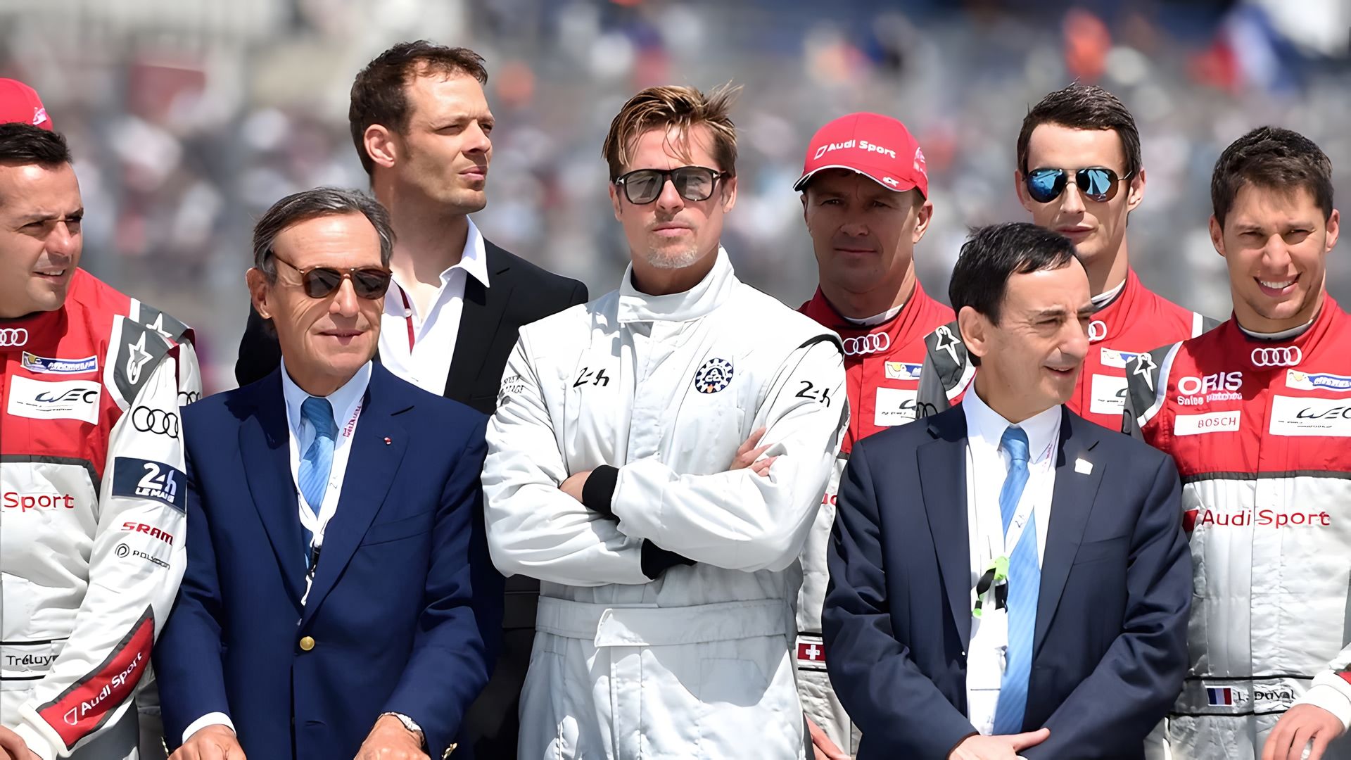 Brad Pitt in equipaggiamento da pilota da corsa circondato dal suo team