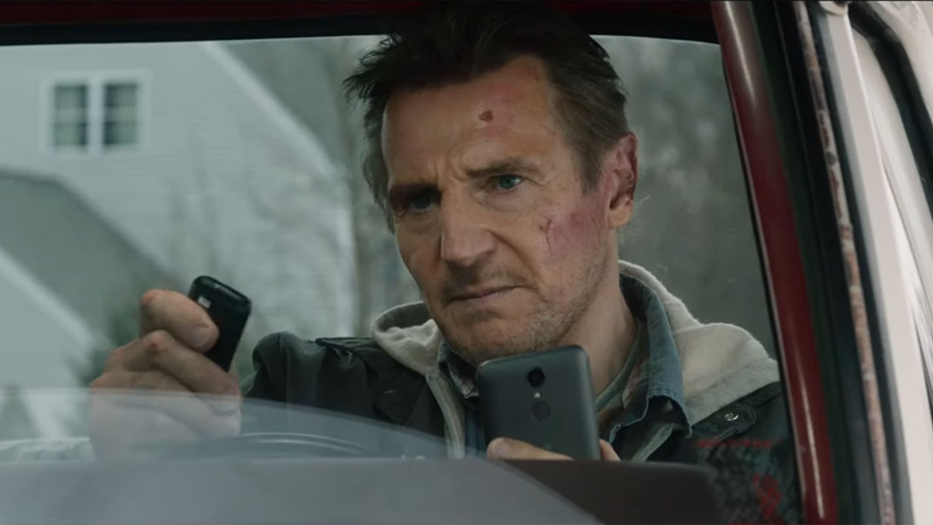 Liam Neeson siede in macchina fissando tensamente il telefono e il telecomando nelle sue mani