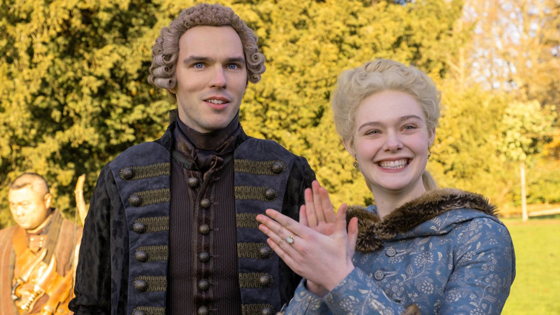 Nicholas Hoult ed Elle Fanning in costumi d'epoca del XVIII secolo in piedi per strada, l'attrice sta sorridendo e battendo le mani