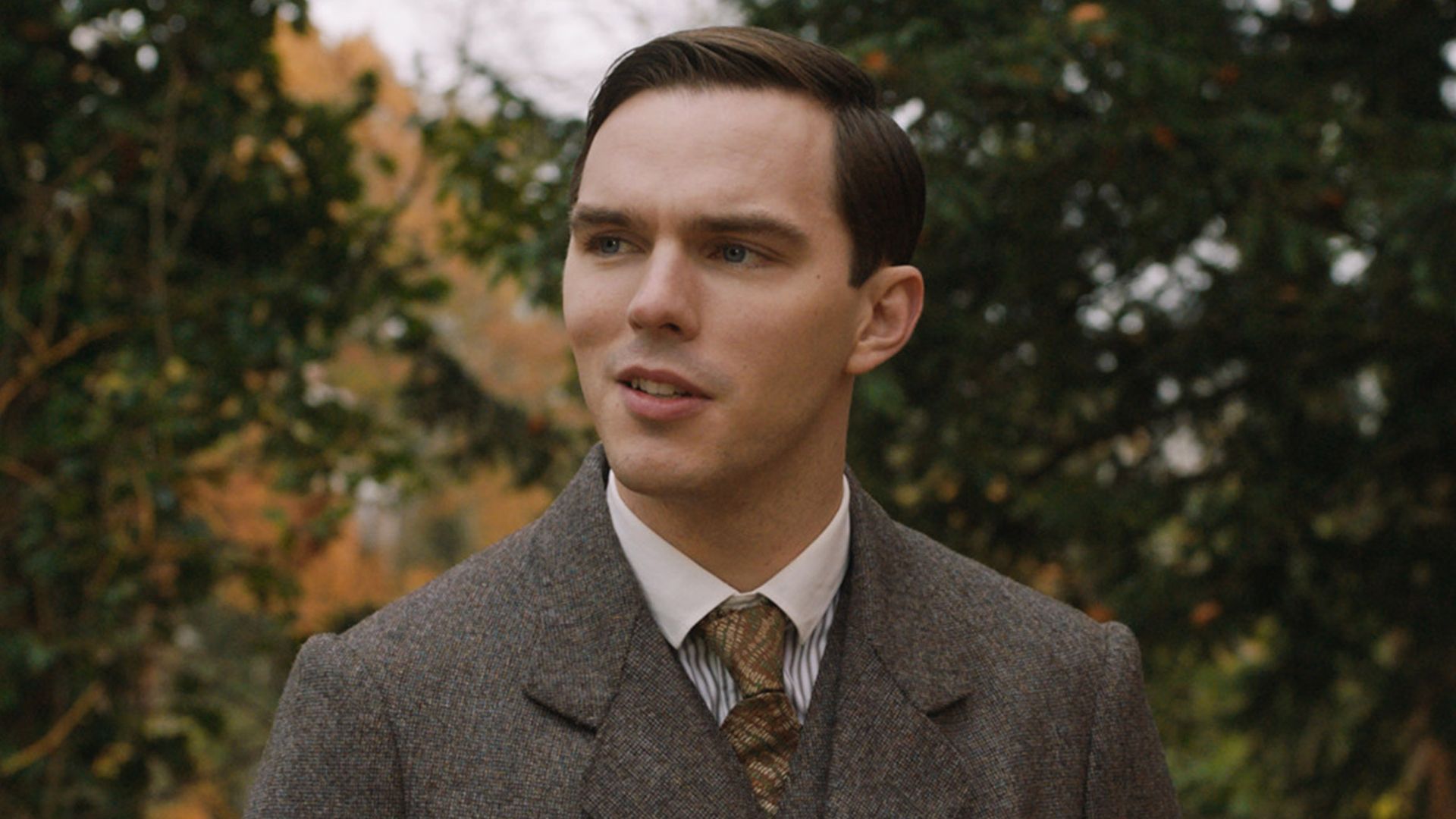 Nicholas Hoult in completo marrone e cravatta in piedi per strada nel ruolo del giovane J.R.R. Tolkien