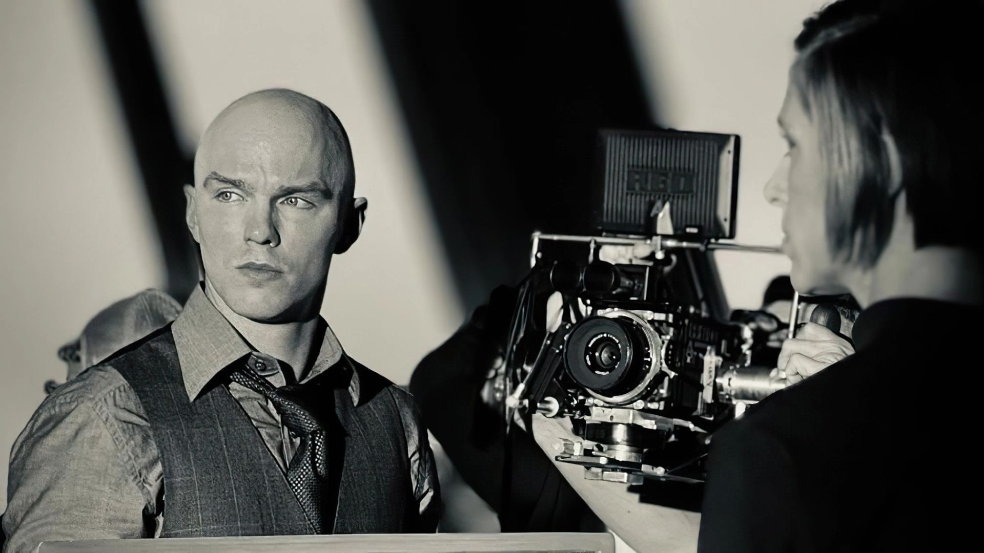 Nicholas Hoult in gilet e cravatta in piedi accanto a una telecamera cinematografica professionale su un set cinematografico
