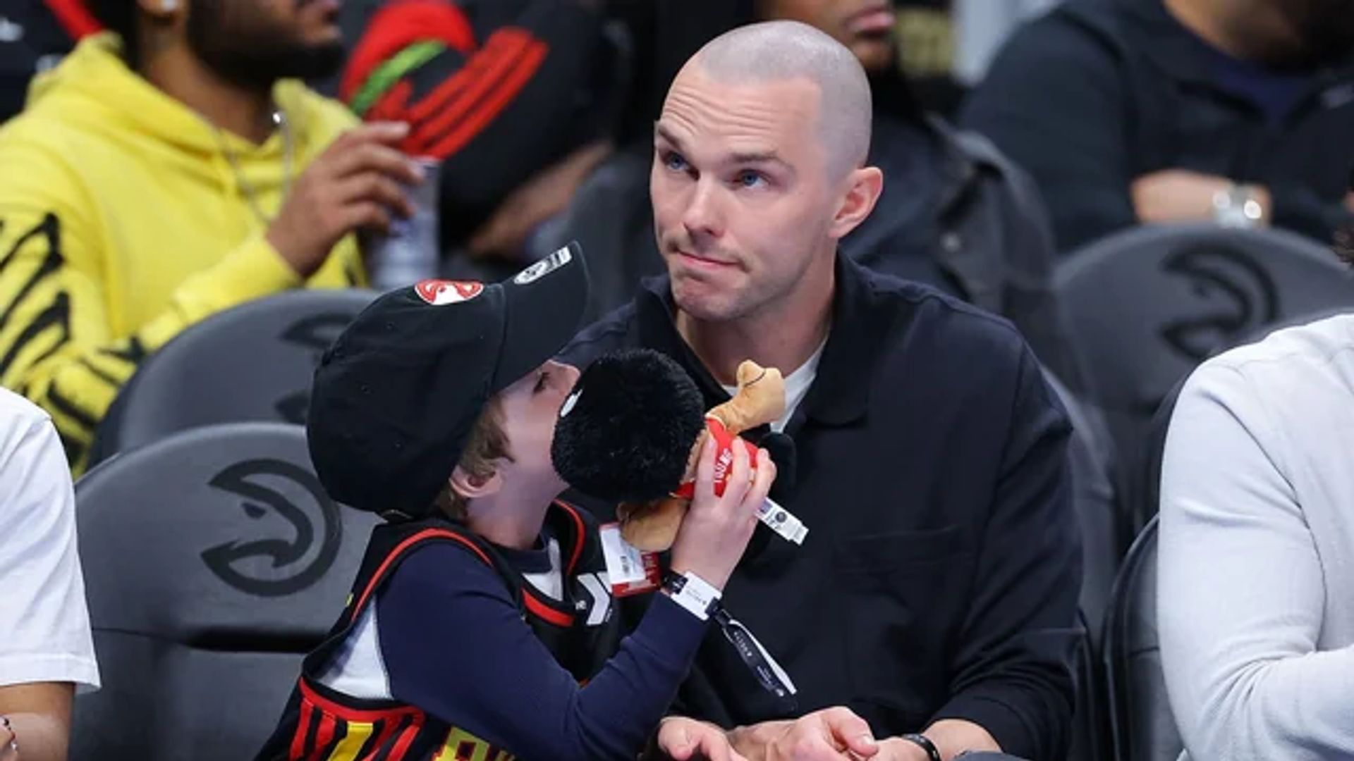 Nicholas Hoult seduto sugli spalti di una partita di basket accanto a suo figlio che tiene in mano un giocattolo