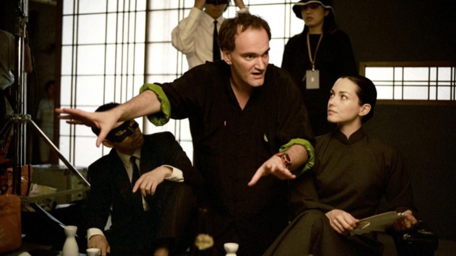 Il regista Quentin Tarantino in abiti neri che dà indicazioni a persone vestite di nero