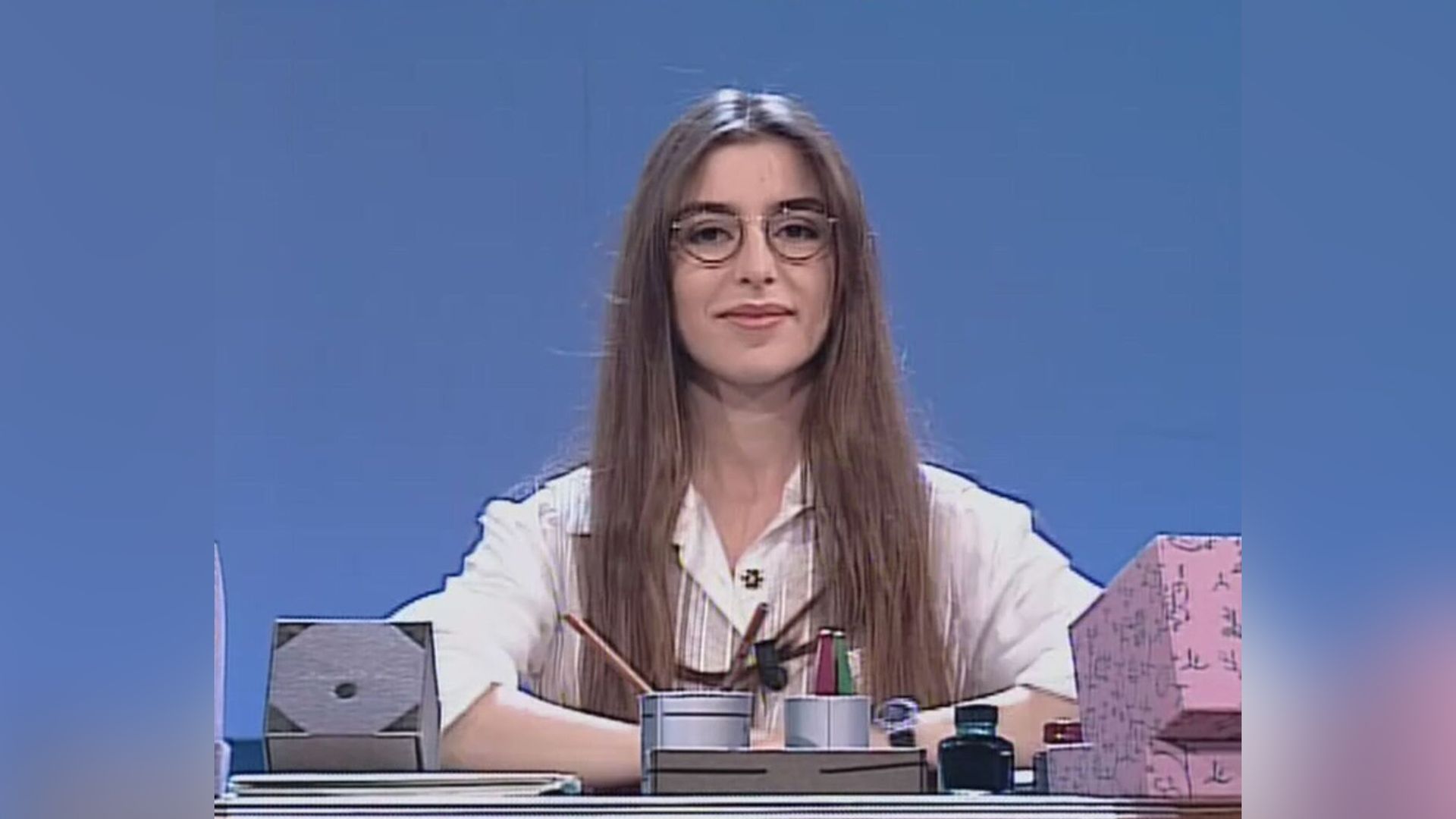 La giovane Sabrina Impacciatore con gli occhiali e una camicetta bianca seduta a una scrivania