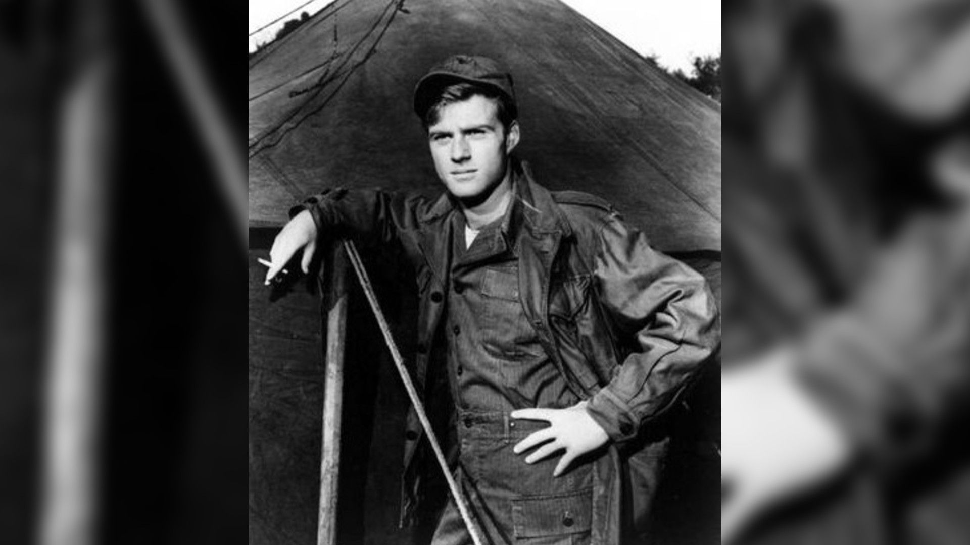 Foto in bianco e nero del giovane Robert Redford in uniforme militare in piedi accanto a una tenda, scena dal film "War Hunt"