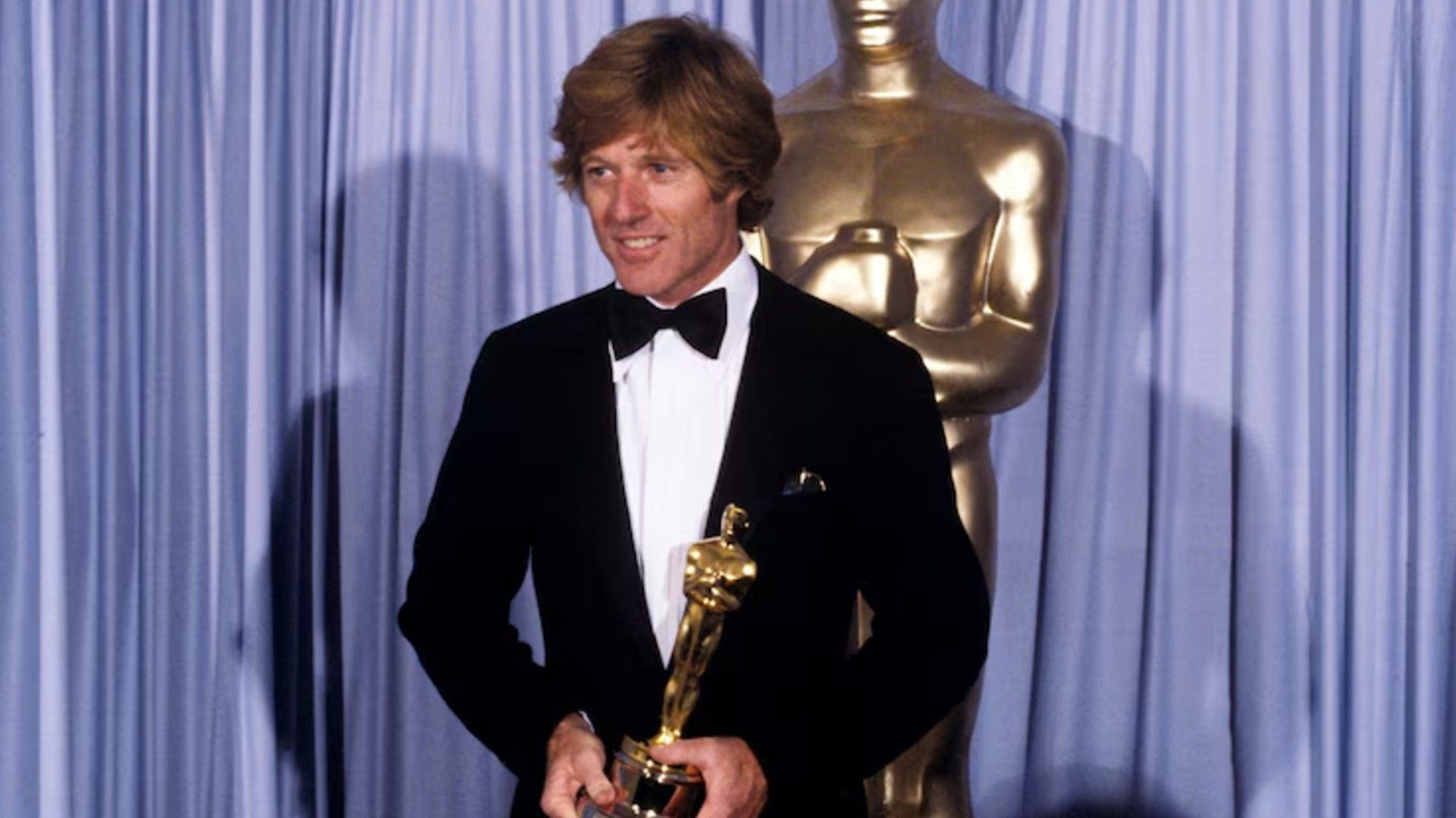 Robert Redford in abito elegante sul palco con in mano un Oscar
