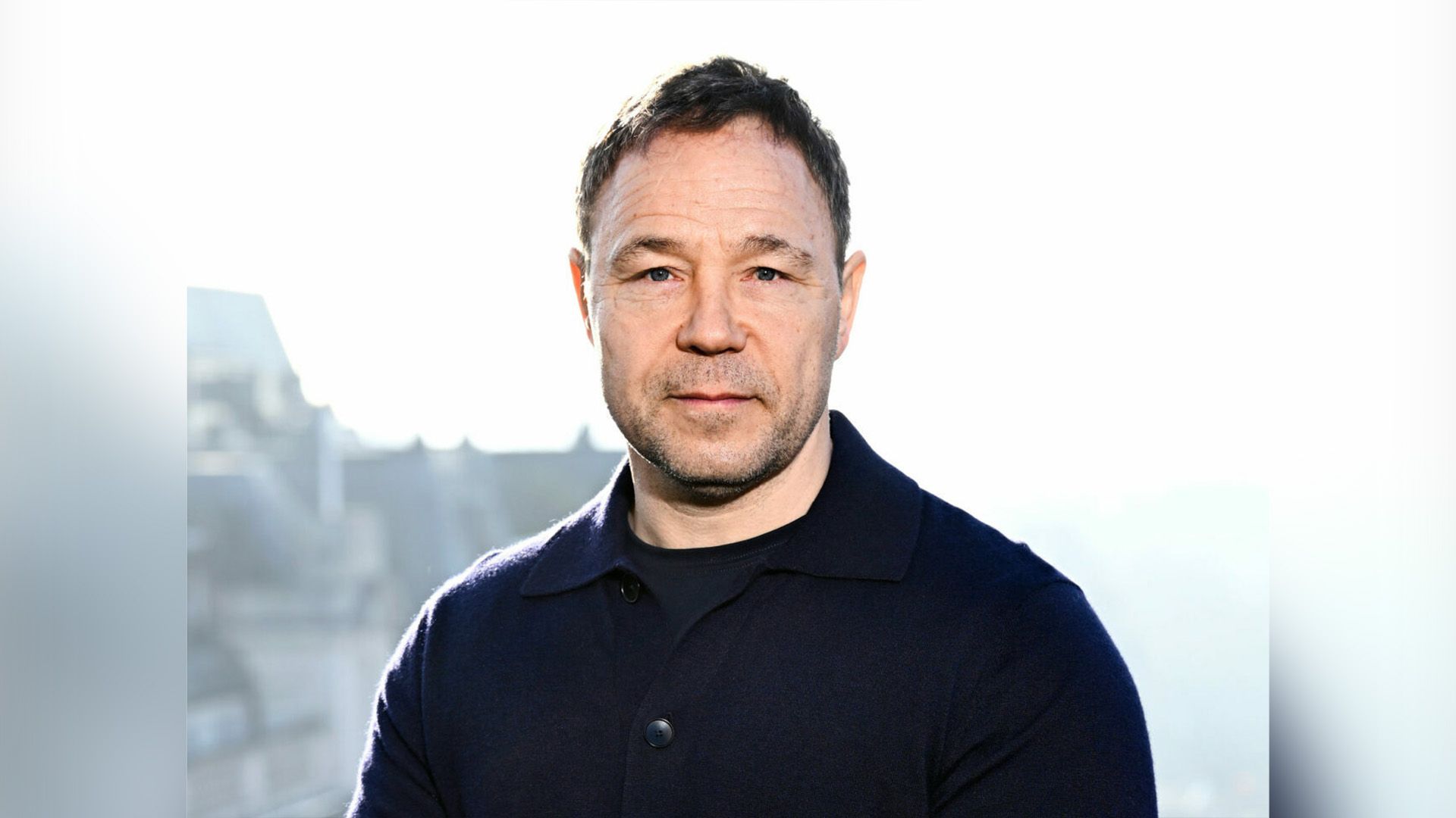 L'attore Stephen Graham con un maglione nero su sfondo bianco