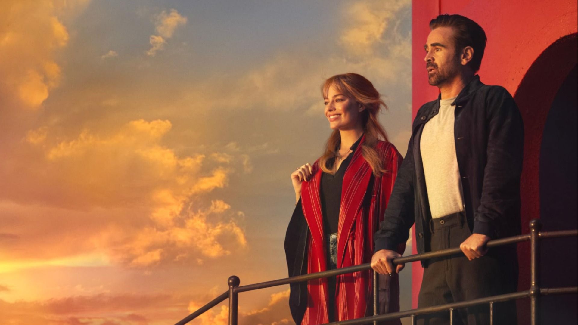 Gli attori Margot Robbie e Colin Farrell in abiti casual sul ponte di una nave mentre guardano il tramonto