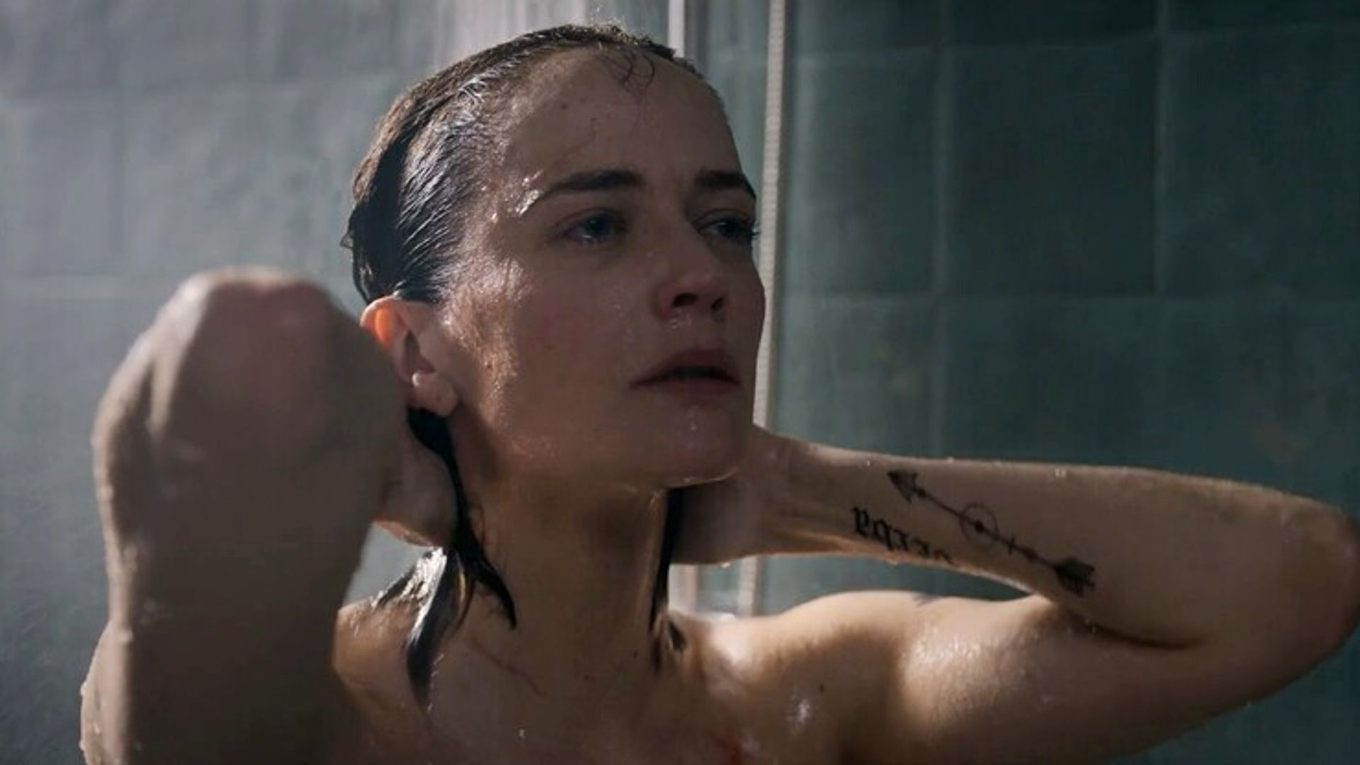Eva Green con i capelli bagnati sotto la doccia, mani dietro la testa, visibili solo il viso e il braccio tatuato