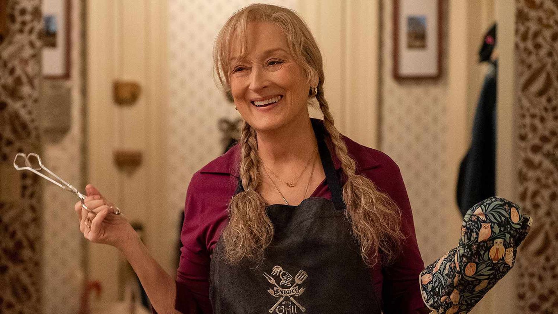 Meryl Streep con le trecce tiene delle pinze in una mano, indossando un guanto da cucina nell'altra
