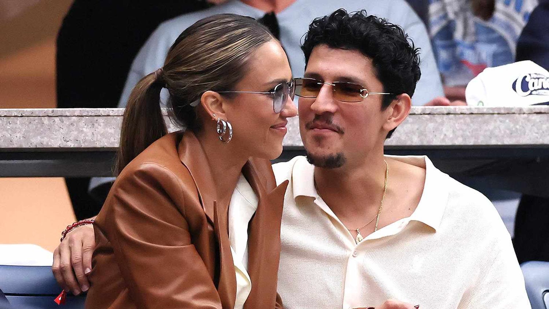 Jessica Alba e Danny Ramirez seduti sugli spalti di un evento sportivo abbracciati