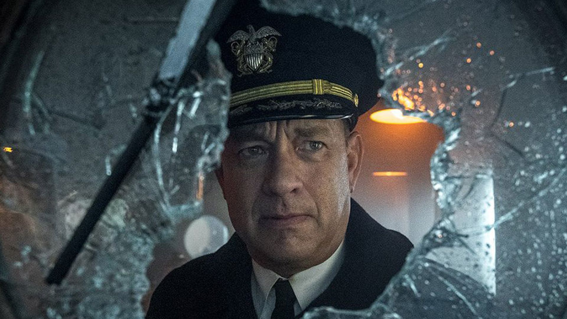 Tom Hanks in uniforme da capitano guarda attraverso un vetro rotto con un'espressione seria sul viso