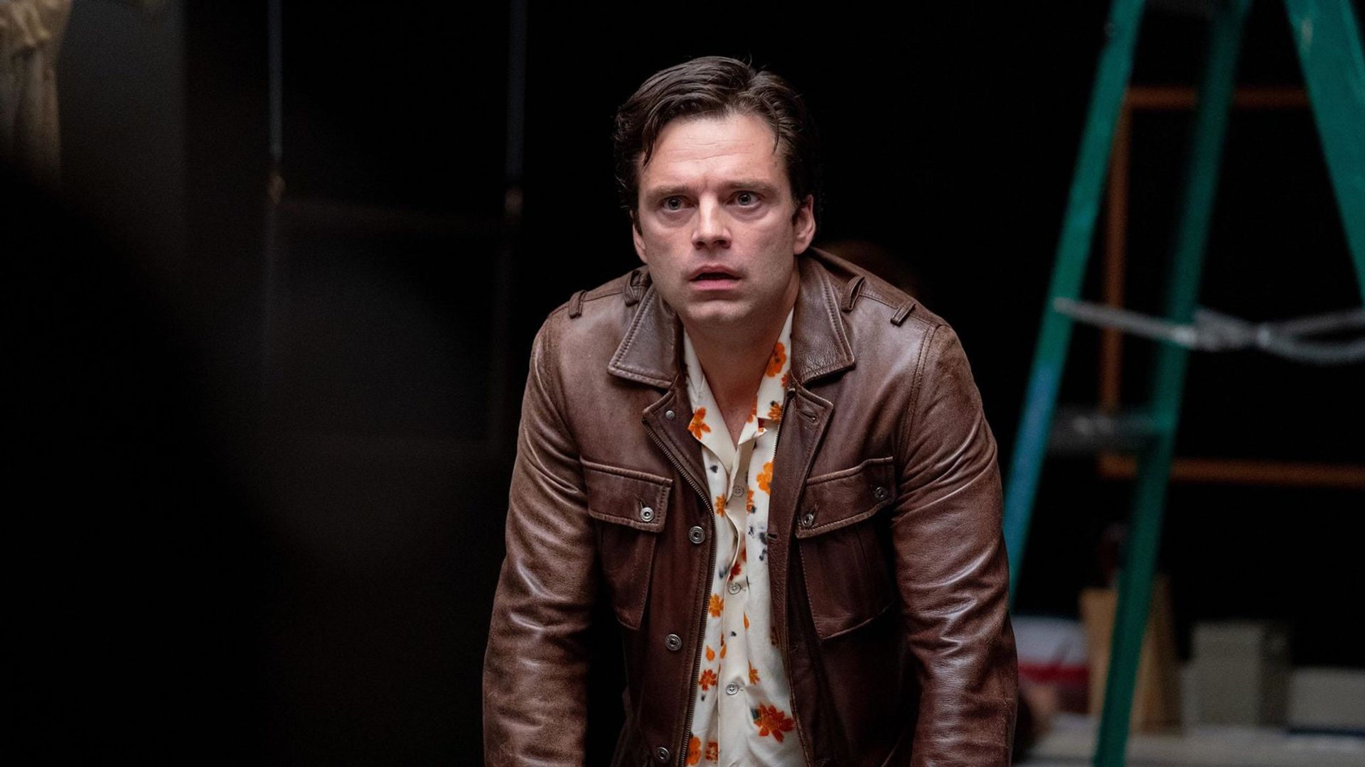 Sebastian Stan con una giacca marrone che guarda avanti su sfondo nero