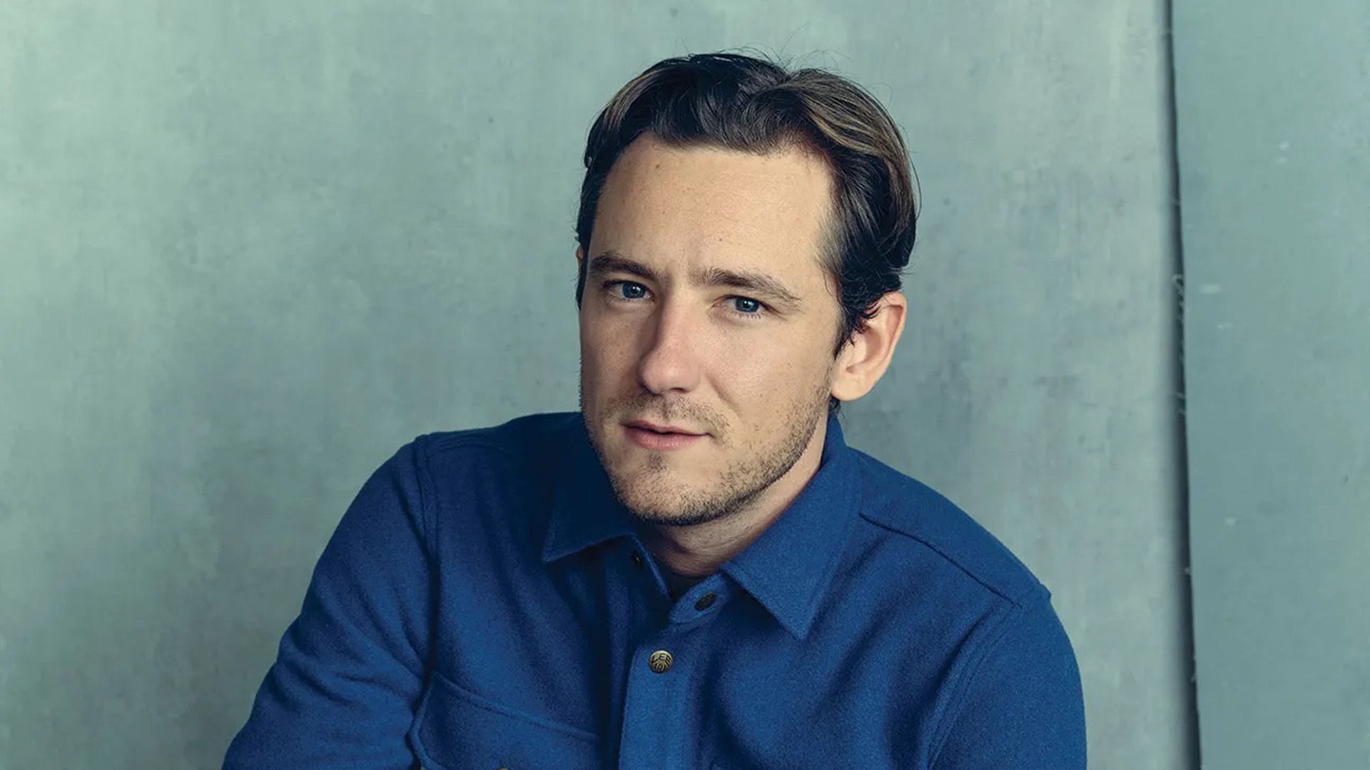 L'attore Lewis Pullman in camicia blu su sfondo azzurro