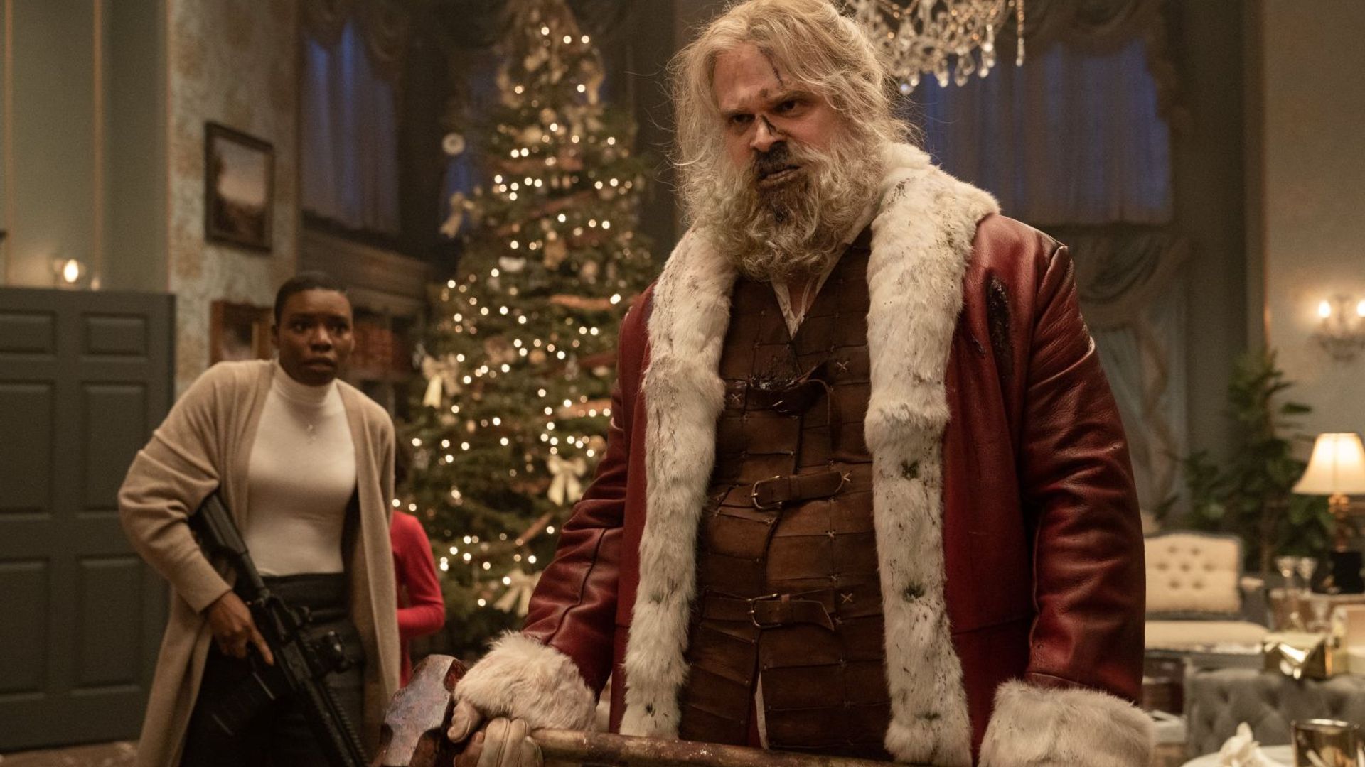 David Harbour in costume da Babbo Natale con un'ascia in mano, con decorazioni natalizie sullo sfondo