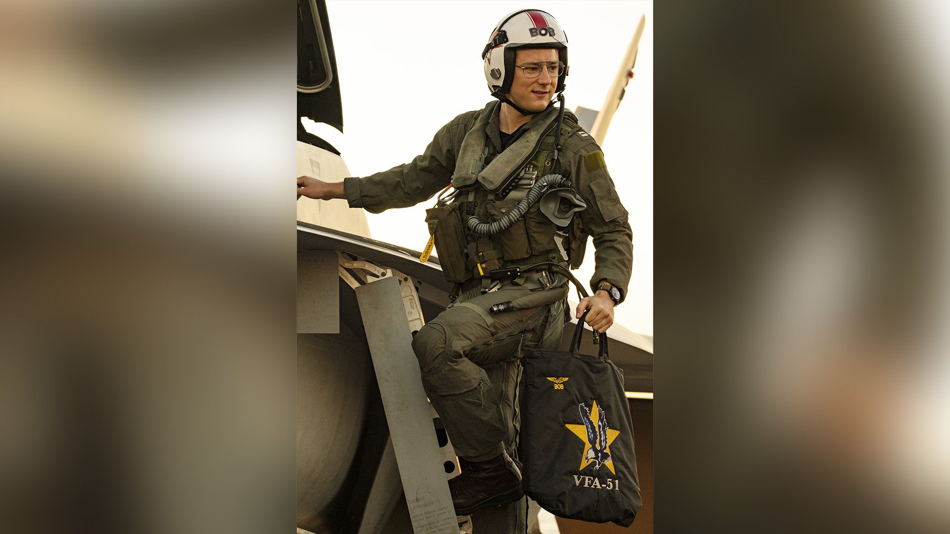 Lewis Pullman in uniforme da pilota militare in piedi sul gradino di un jet da combattimento