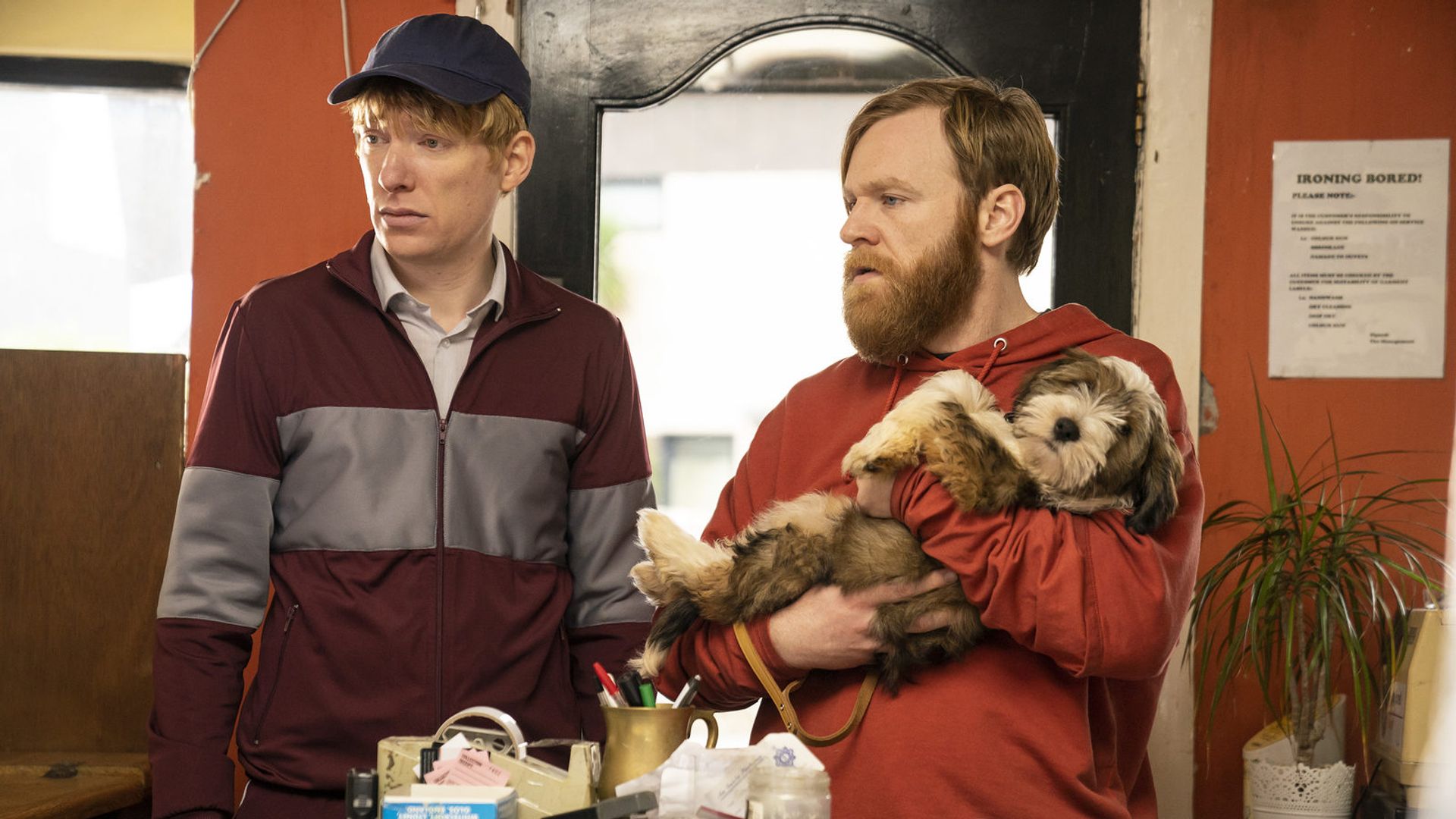 Brian e Domhnall Gleeson in abbigliamento sportivo in piedi vicino a un tavolo che guardano di lato