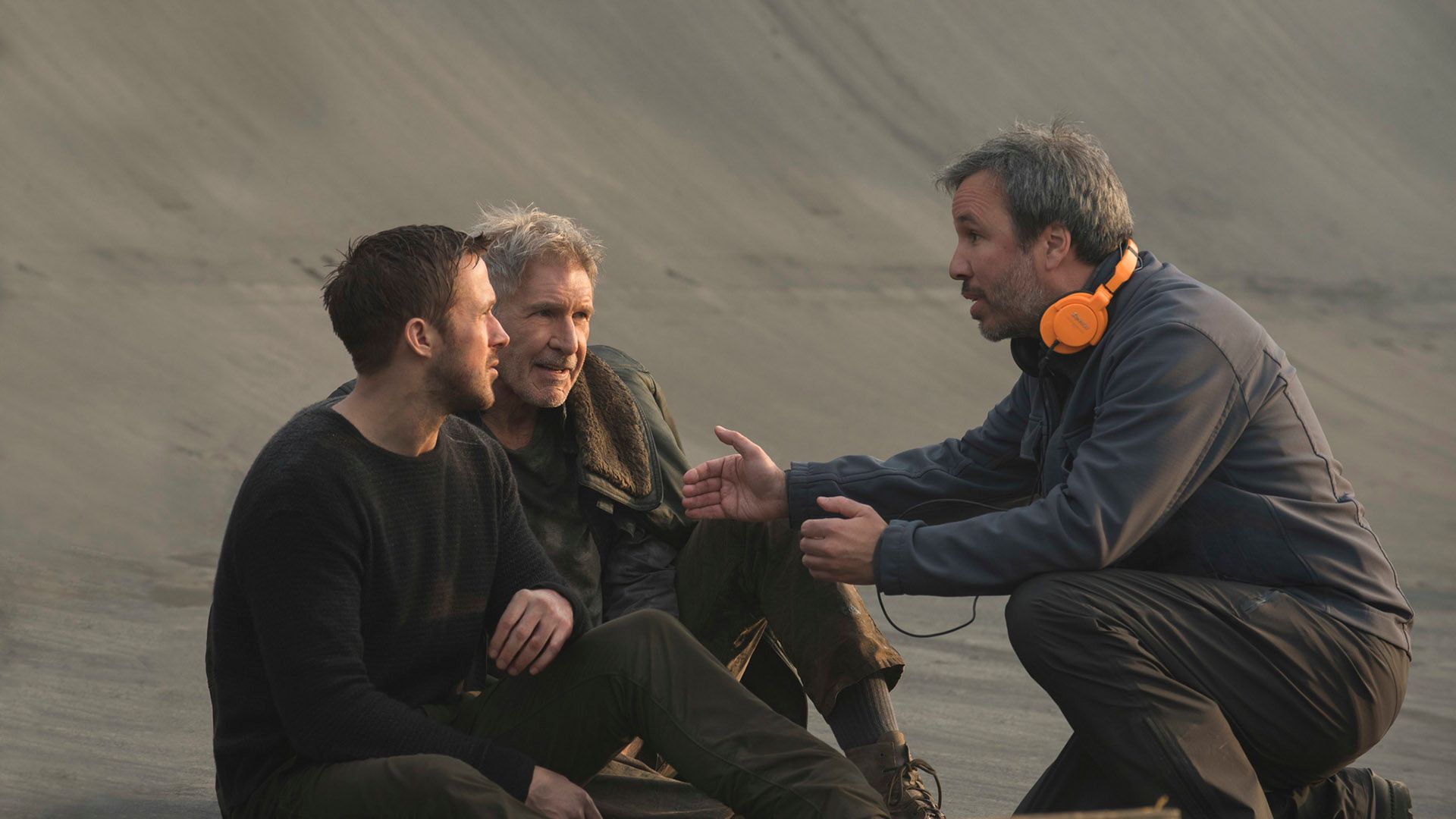 Denis Villeneuve, gesticolando, spiega qualcosa a Ryan Gosling e Harrison Ford seduti davanti a lui