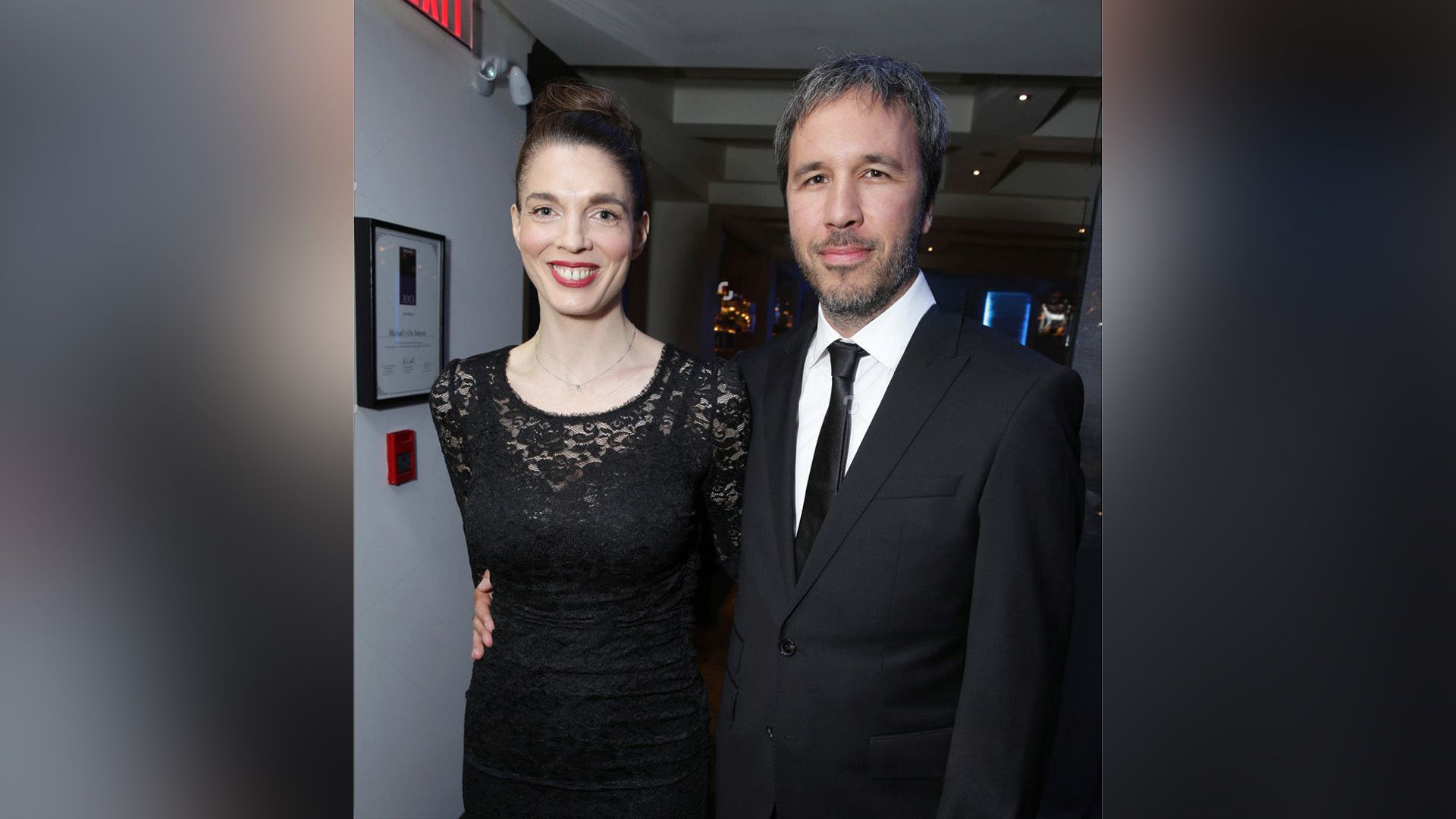 Denis Villeneuve in completo abbraccia una sorridente Masha Grenon in un vestito di pizzo nero intorno alla vita