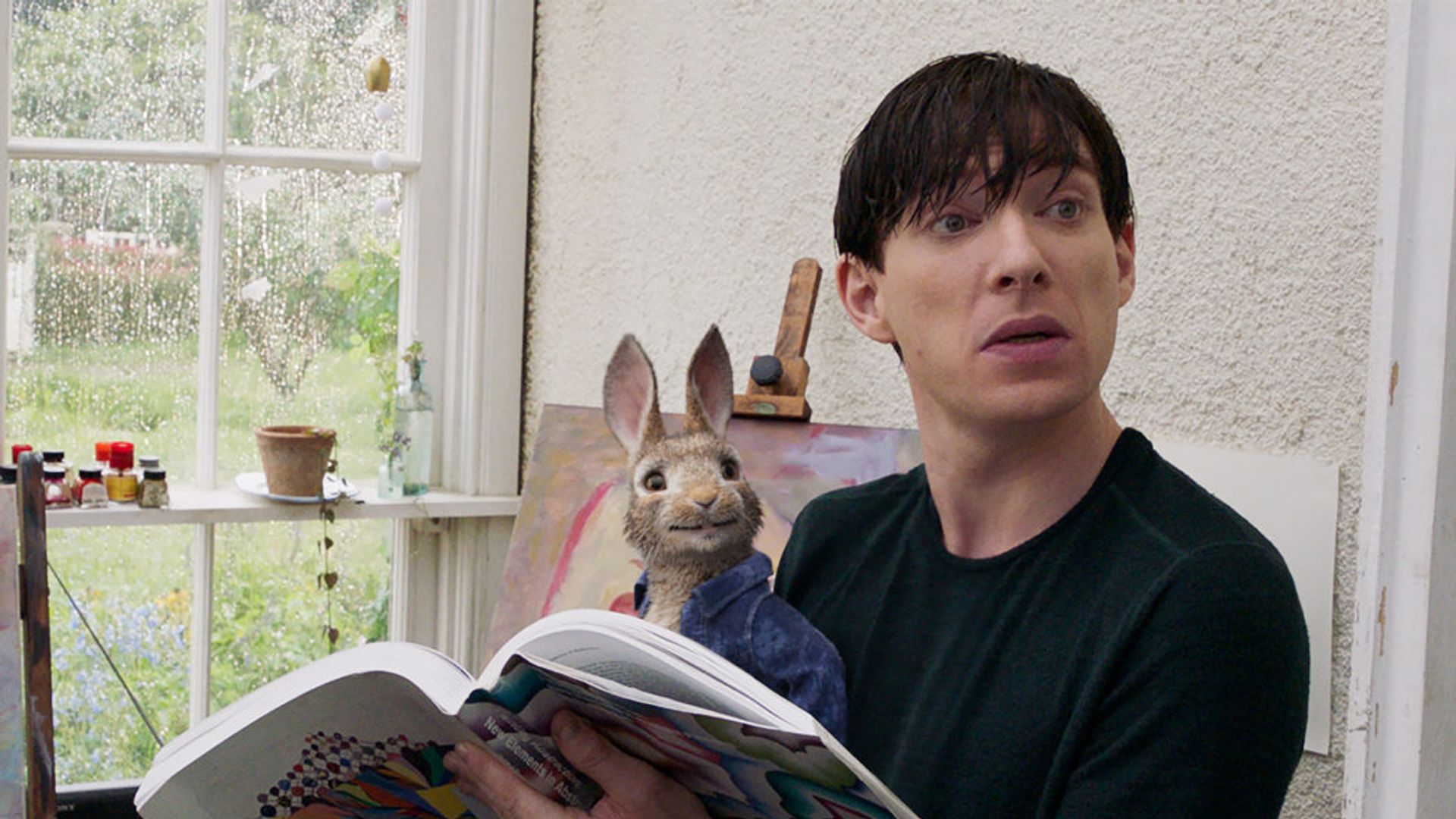 Domhnall Gleeson seduto che legge un giornale con un coniglietto giocattolo sulle ginocchia