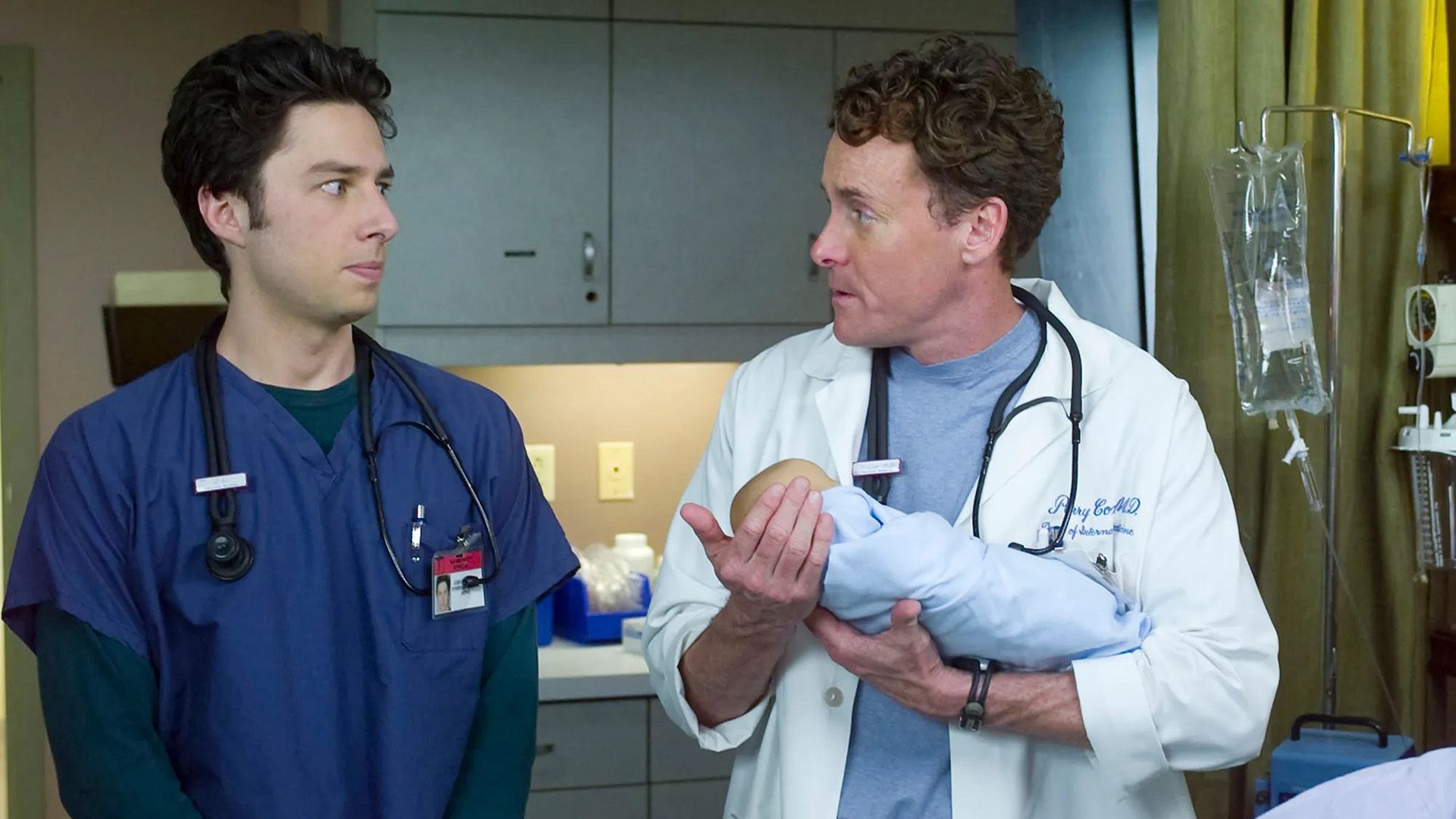 John C. McGinley in camice bianco tiene in braccio un neonato, con Zach Braff nelle vicinanze in camice azzurro