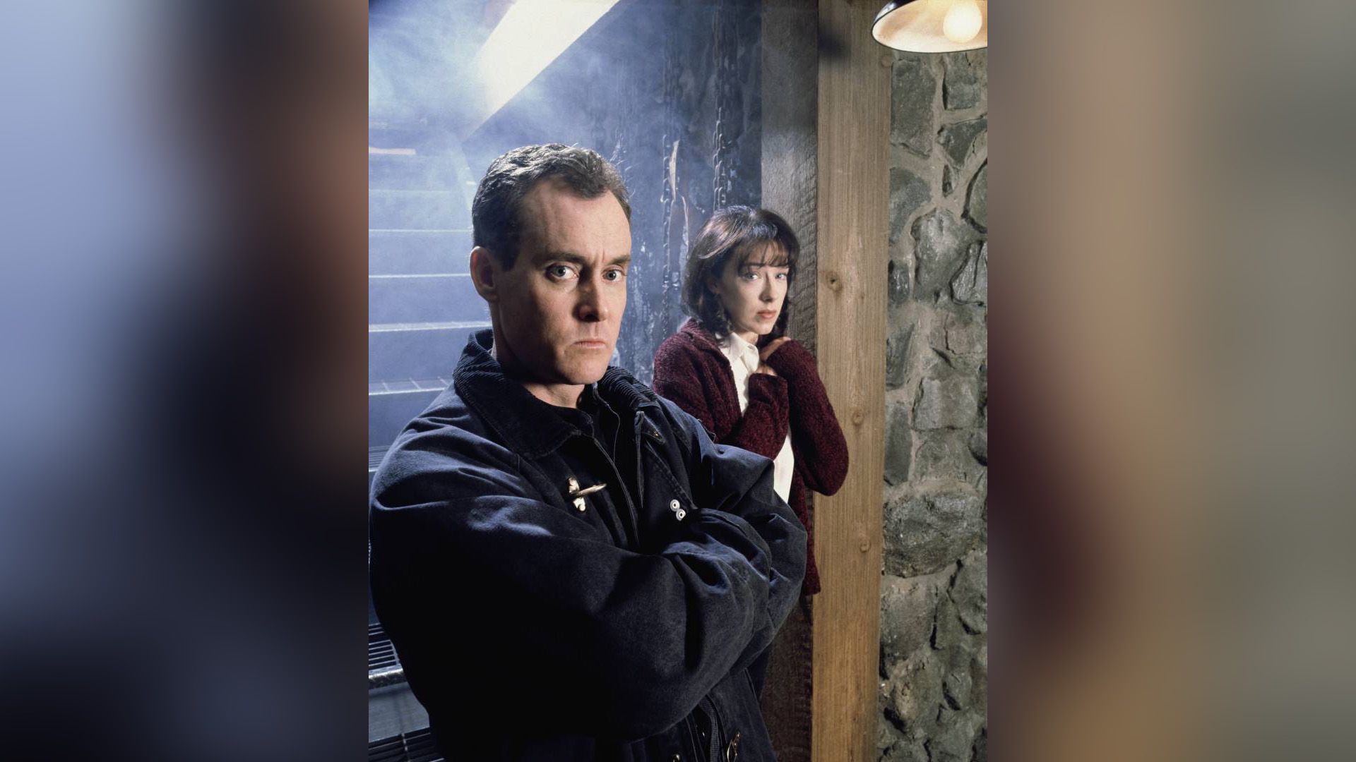 John C. McGinley con un'espressione seria in piedi vicino a una scala con una ragazza spaventata dietro di lui