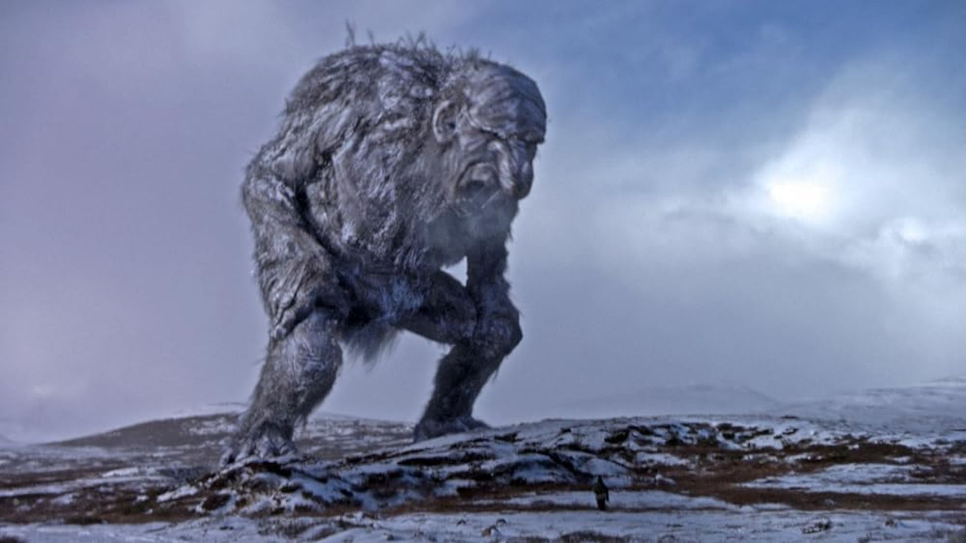 Un mostro umanoide grigio e massiccio si erge su una strada innevata